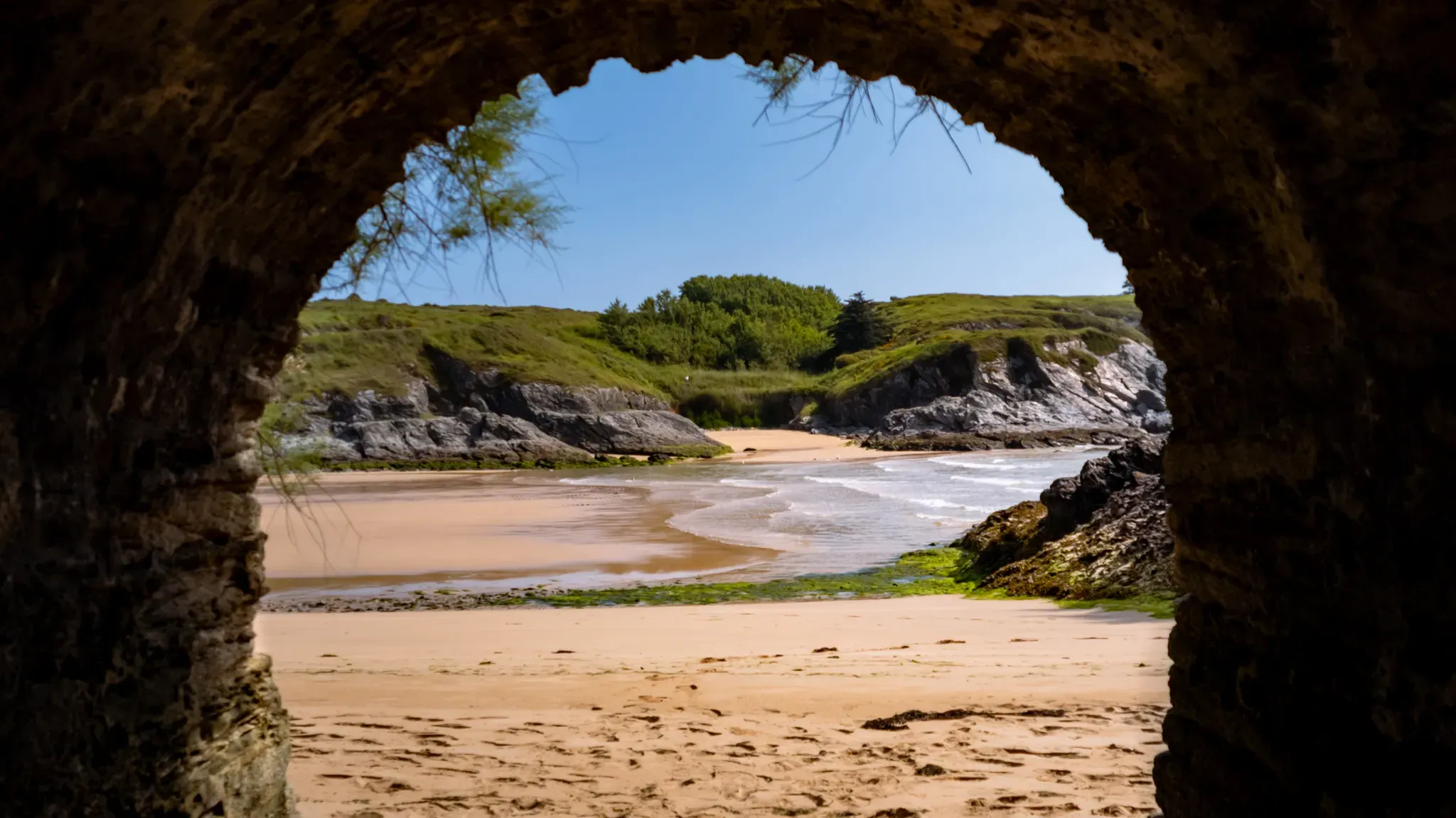 Vue sur une plage de Belle-Île-en-Mer encadrée par une arche rocheuse sombre