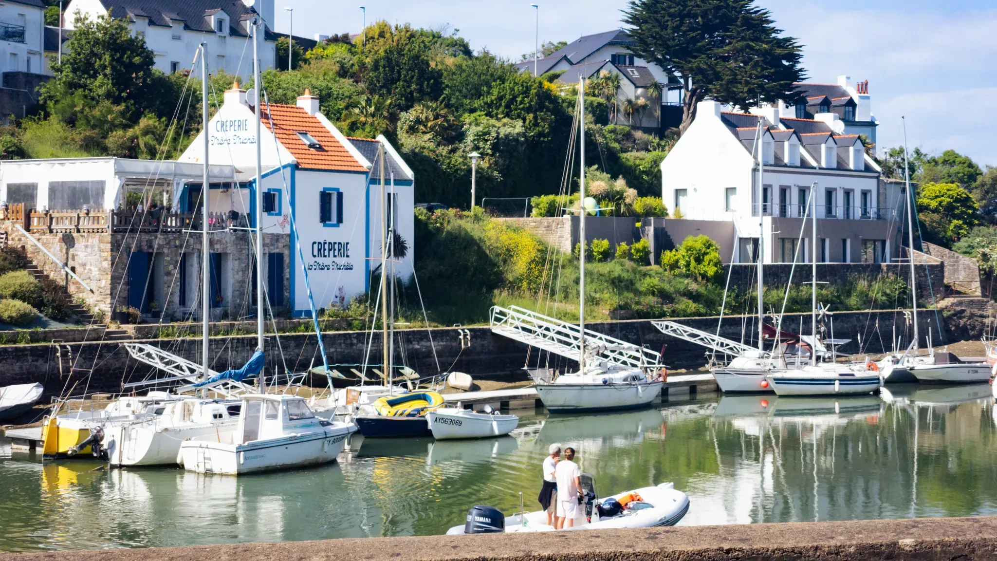 Voiliers amarrés dans un petit port de Belle-Île-en-Mer, entouré de maisons blanches et de végétation.