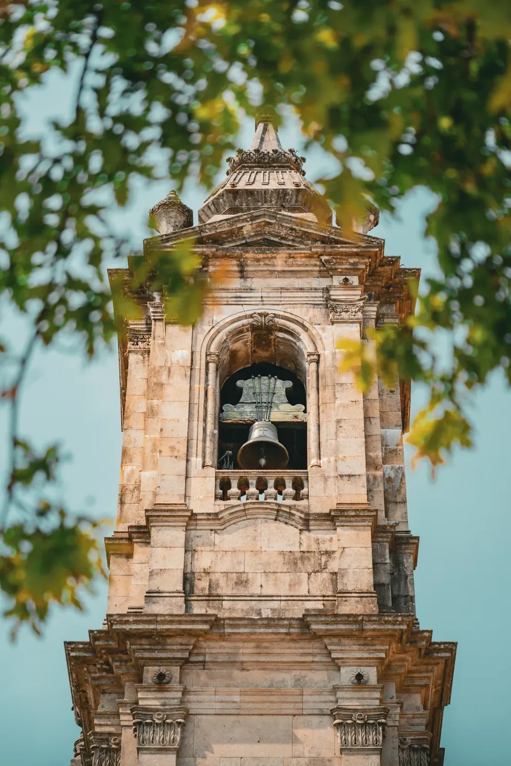 Photographie d un clocher de Braga encadre par des feuilles d arbre.