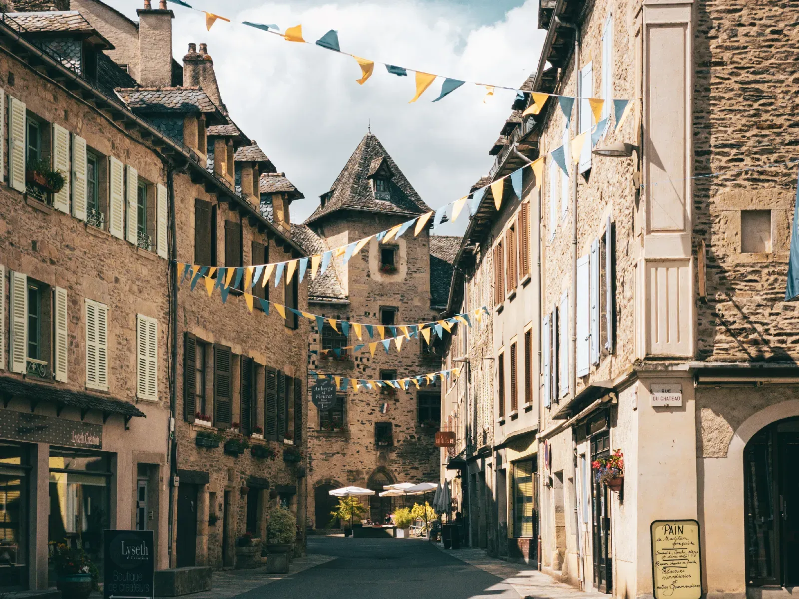 Rue du village d’Estaing bordée de maisons en pierre et décorée de fanions colorés.