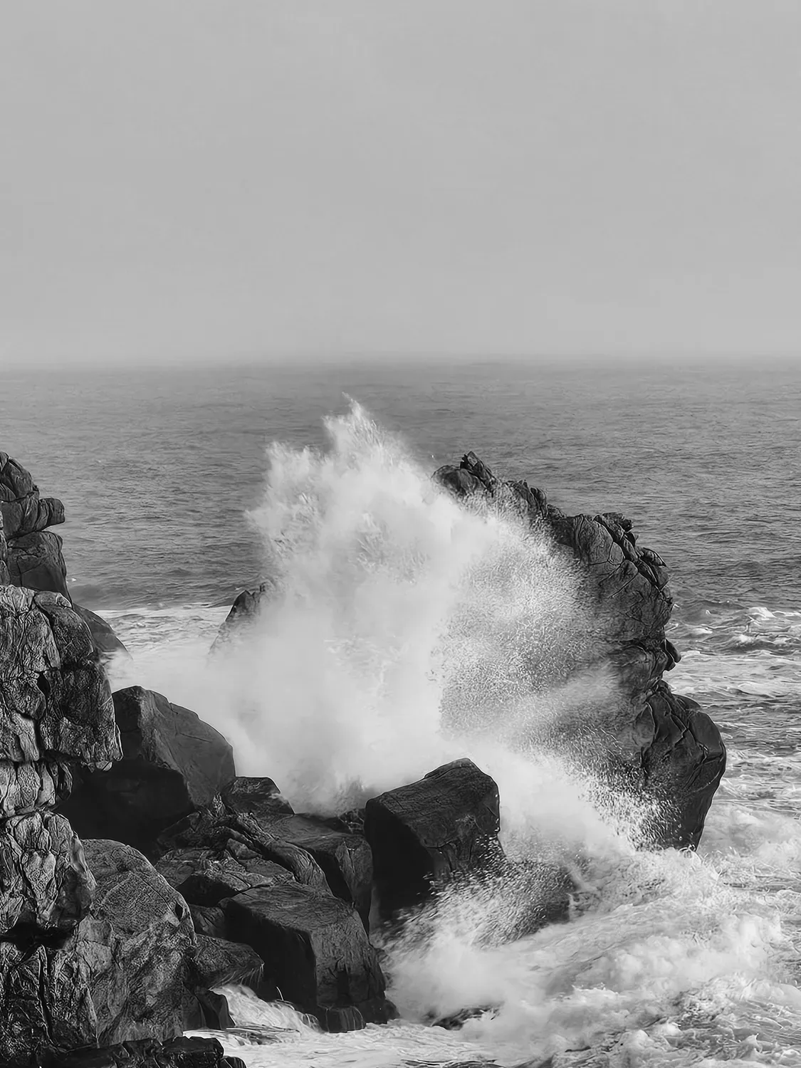 Photographie en noir et blanc de vague contre les rochers.