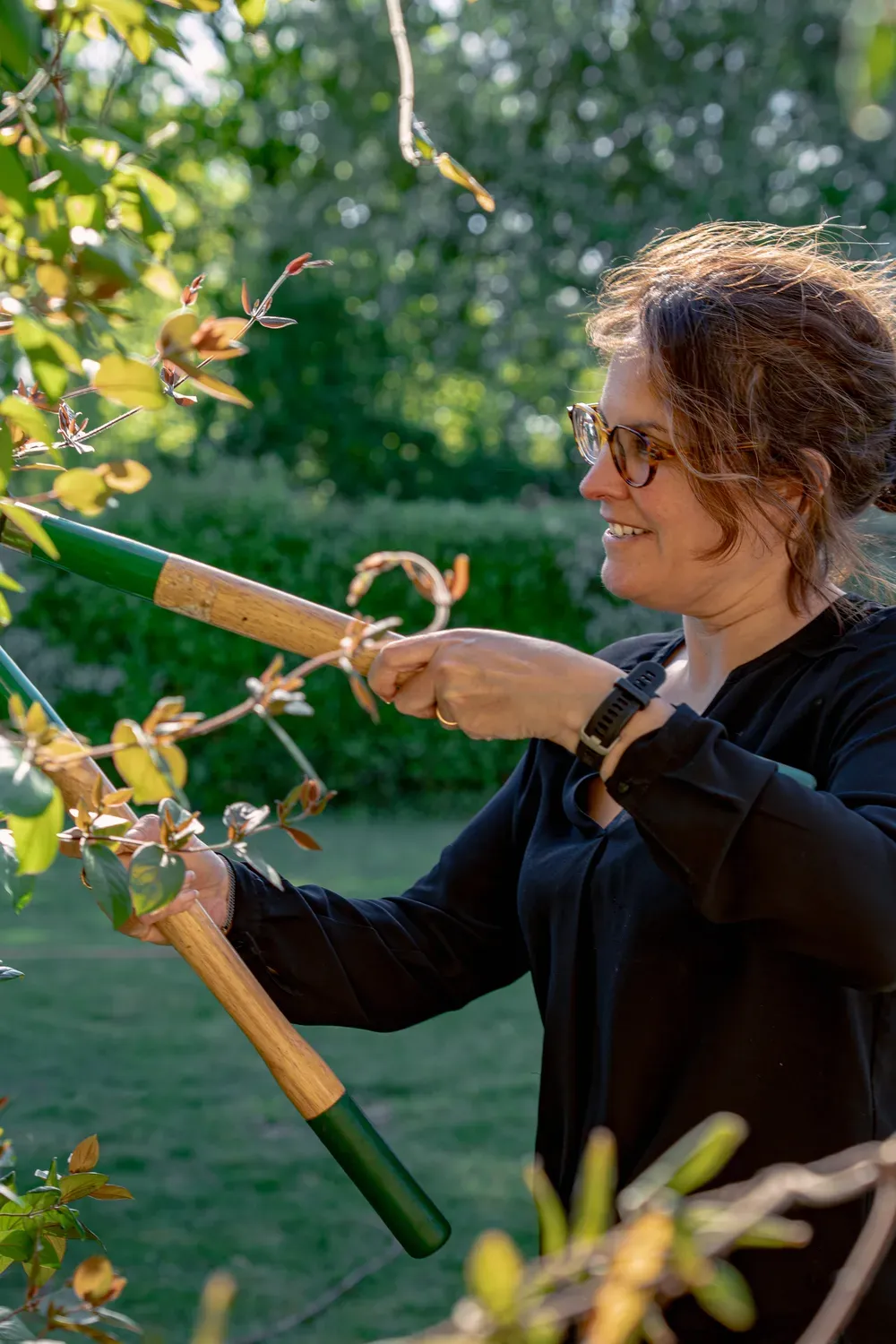 Photographie d une femme qui taille des branches avec un coupe-branche.