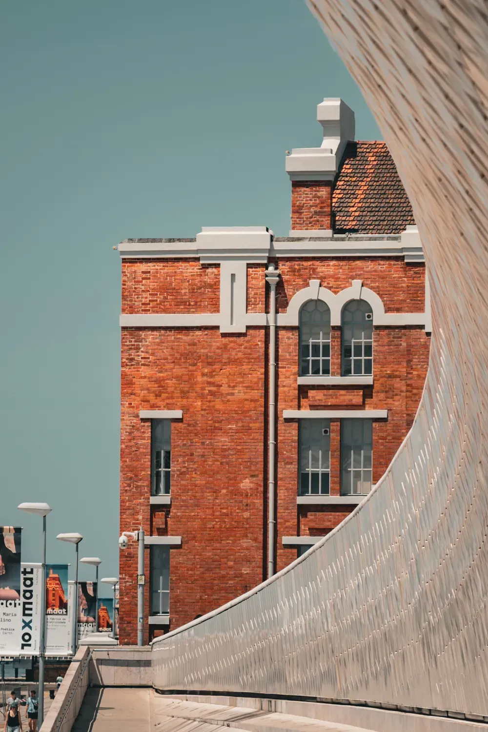 Photographie verticale de la courbe blanche du MAAT devant une facade en brique.