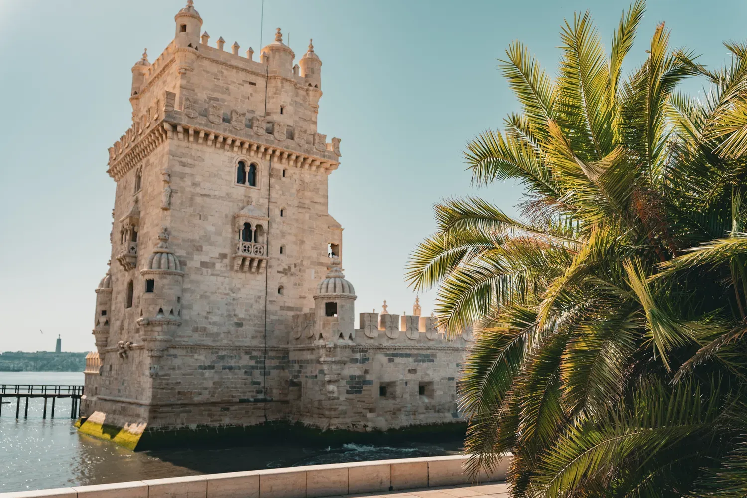 Photographie de la tour de Belem au bord du Tage avec un palmier au premier plan.