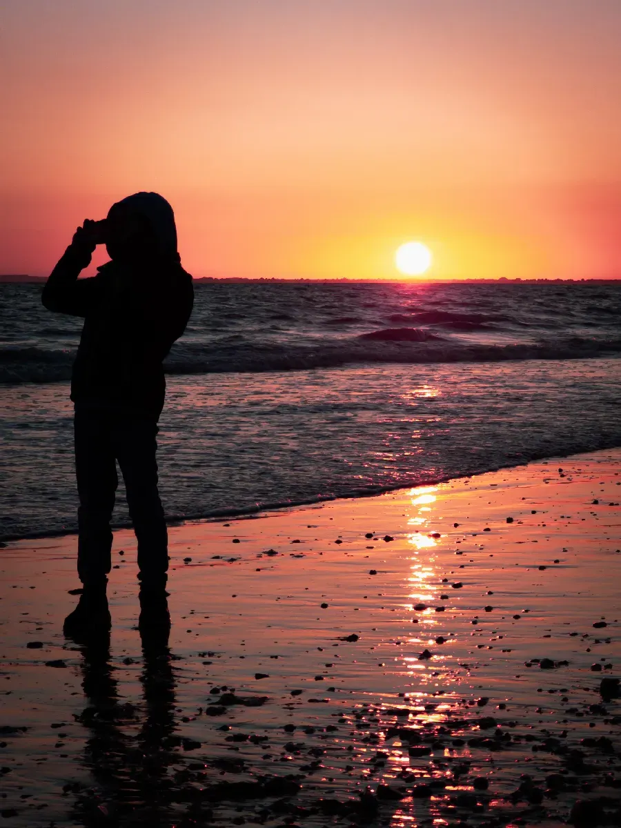 Silhouette d’une personne sur la plage face au soleil couchant.