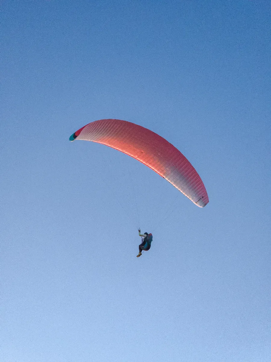Parapentiste sous une voile rose éclairée par le soleil, évoluant dans un ciel bleu.
