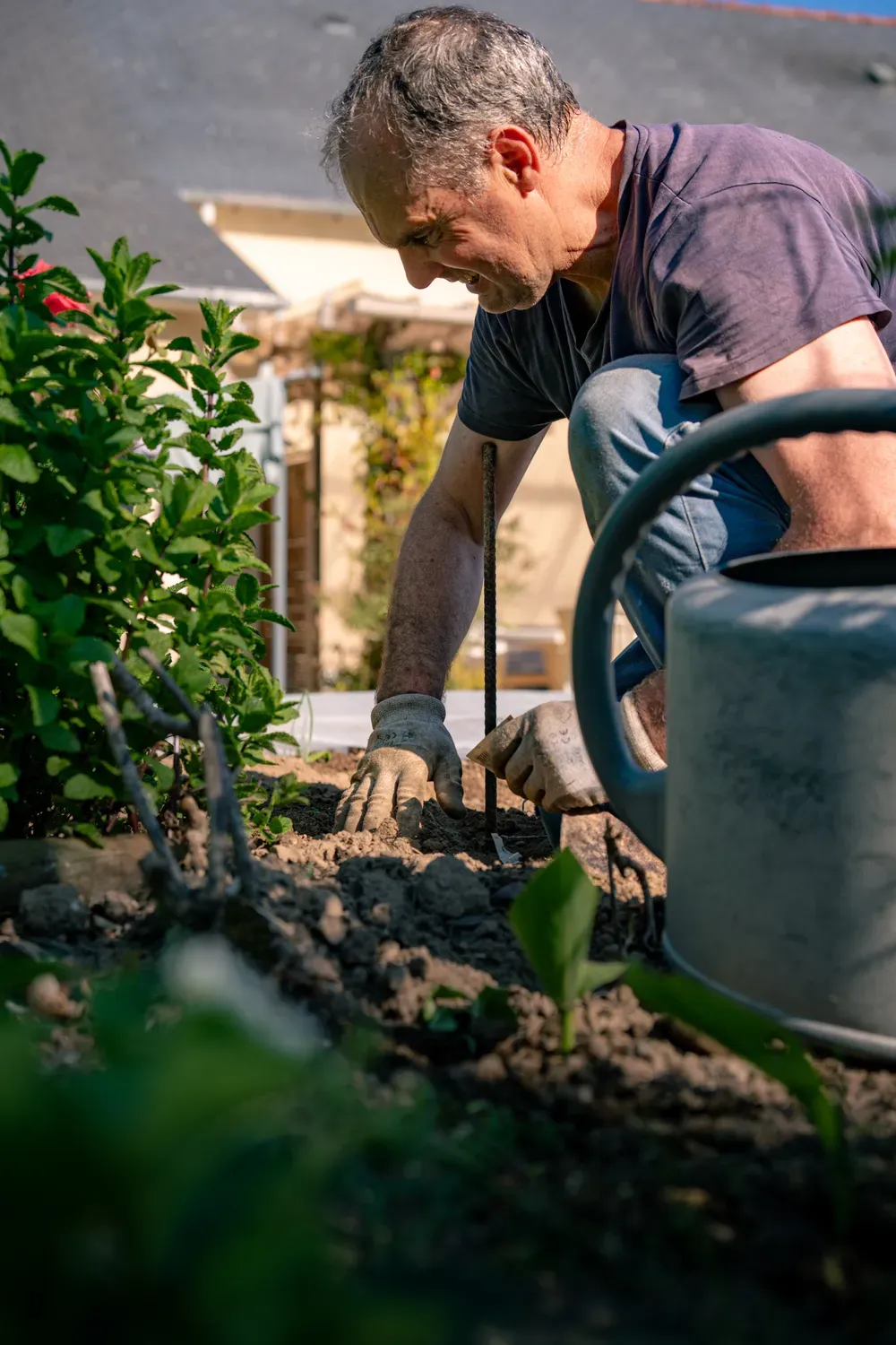 Photographie d un homme qui prepare la terre d un jardin avec des outils.