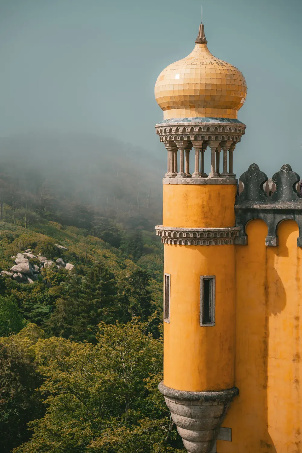 Photographie d une tour jaune du palais de Pena avec la foret embrumee en arriere-plan.