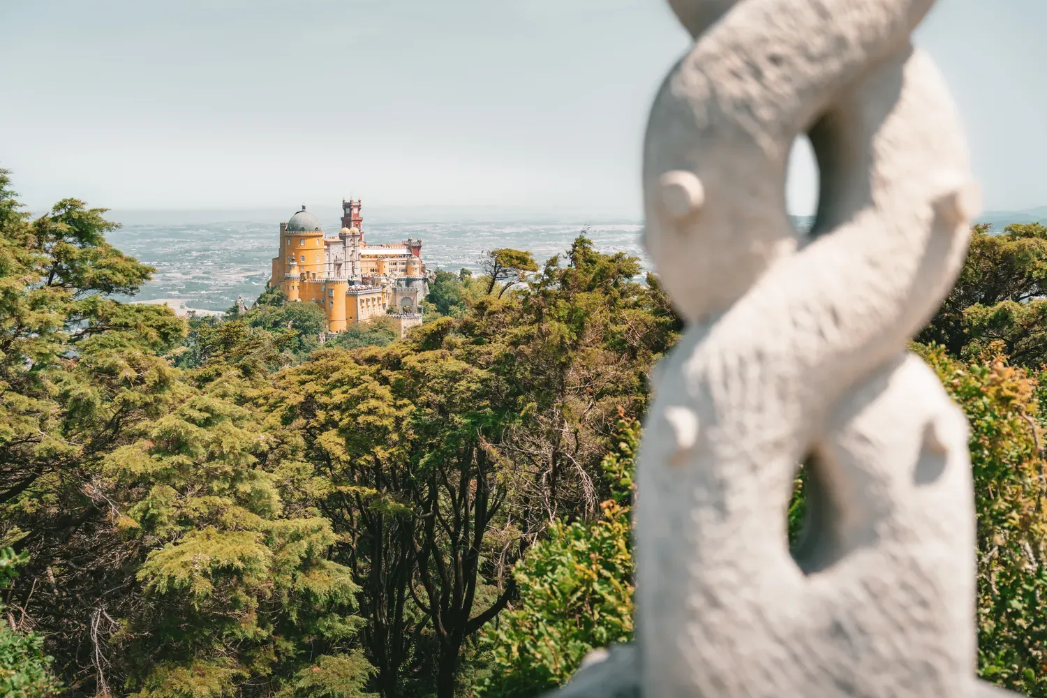 Photographie du palais de Pena visible au-dessus de la foret de Sintra.